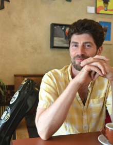 Stephen Guerra sits at a caf&eacute; table beside his instrument case. 