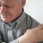 An elderly man holds his shoulder in pain. 