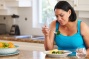 A frustrated or disappointed-looking woman eating a healthy meal including broccoli in a kitchen setting. 