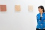 Millie Chen stands next to and looks at her artwork hung in a gallery. 