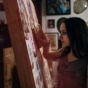 Sideview of Molly Crabapple working on a painting. 