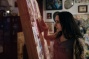 Sideview of Molly Crabapple working on a painting. 