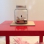 A clear jar filled with scraps of paper sits on a square table. 