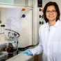 Diana Aga stands in a lab in a white coat. 