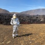 Martin Harris stands in a silver heat-protective suit holding a field rheometer prototype in front of a lava flow at Litli-hrútur in Iceland. 