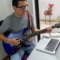 Man playing guitar, laptop open on a table in front of him. 