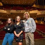 Julia Miskines, Jamie Enser, and Aidan Clarke stand on the CFA Mainstage with their back to the audience seating. 