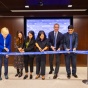 six people standing next to each other cutting blue UB ribbon. 