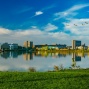 UB campus buildings over lake with blue sky and geese flying overhead. 