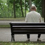 An elderly man sitting alone on a park bench. 