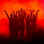 Silhouetted dancers stand in a line with arms raised in elegant, expressive poses against a vibrant red and orange illuminated background, creating a dramatic and artistic effect. 