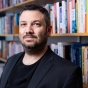 Yotam Ophir stands in front of a shelf full of books. 