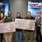 Five people stand together smiling and holding two oversized award checks after a criminology design challenge. The pair on the left holds a check for $750 labeled &ldquo;Second Place &ndash; Rise Above,&rdquo; and the pair in the center and right holds a check for $1,000 labeled &ldquo;First Place &ndash; Operation Kops.&rdquo;. 