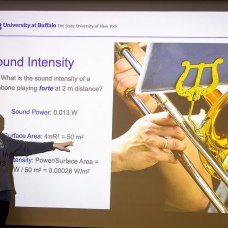 Benedikt Harrer points to a large screen depicting a person playing a brass instrument during his Physics of Sound class. 