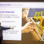 Benedikt Harrer points to a large screen depicting a person playing a brass instrument during his Physics of Sound class. 