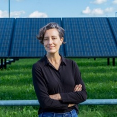 Holly Buck stands outdoors in front of a row of solar panels. 