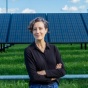 Holly Buck stands outdoors in front of a row of solar panels. 