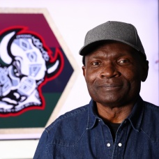 George Afedzi Hughes stands in front of his redesigned Buffalo Sabres &ldquo;goathead&rdquo; logo featuring Pan-African colors and African symbols for Black History Month. 