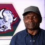 George Afedzi Hughes stands in front of his redesigned Buffalo Sabres &ldquo;goathead&rdquo; logo featuring Pan-African colors and African symbols for Black History Month. 