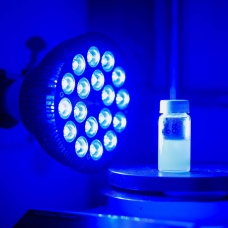 A lamp with over a dozen small blue bulbs shines at vial of light blue liquid. 