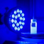 A lamp with over a dozen small blue bulbs shines at vial of light blue liquid. 