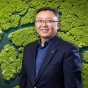 Le "Leo" Wang pictured with an aerial view of a river system in a mangrove forest in the background. 