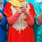 Three women wearing ornate South Asian-style dresses and looking at smart phones. 