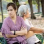 An elderly Chinese woman in her 70s sitting with her adlut child outside. 