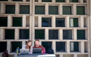 two students studying outside on laptops. 