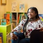 Mirna Cadet is seated in a cozy, brightly lit reading area. 