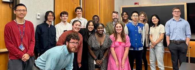 The students from Integrating PPE (PHI 485), spring 2023, stand together in a classroom with their professor.