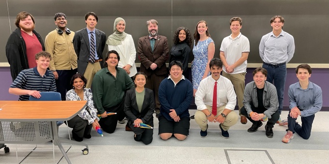 The students from Integrating PPE (PHI 485), spring 2025, stand together in a classroom with their professor.