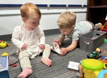 An infant and a toddler play with toys on the ground as part of the study.