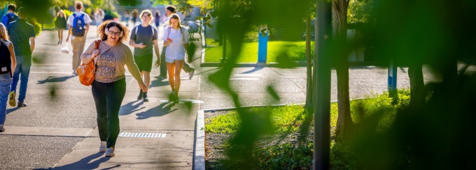 Students walking on a UB campus sidewalk with trees around.