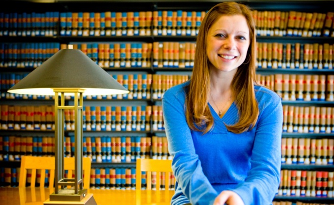 Student sitting on library table in front of book shelves. 