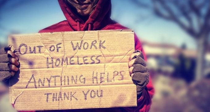Person holding cardboard sign asking for help due to homelessness.