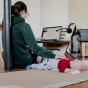 A women working on her laptop and watching over a baby. 