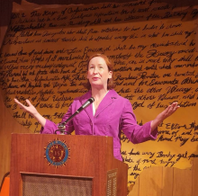 Professor Hunter as a character standing in front of a podium with the US Constitution projected on the wall behind her. 