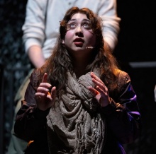 female student with hands raised looks upward onstage. 