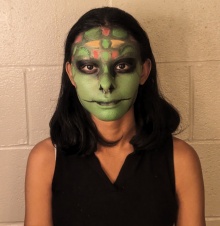 Female student of color in green, red, yellow, black snake makeup. 
