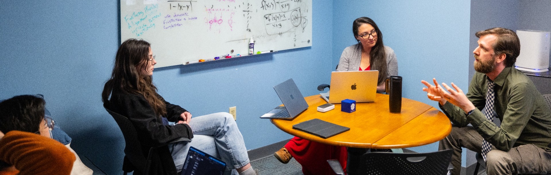 Alexandra Oprea and Ryan Muldoon, both with the Department of Philosophy, meet with students in a conference room.