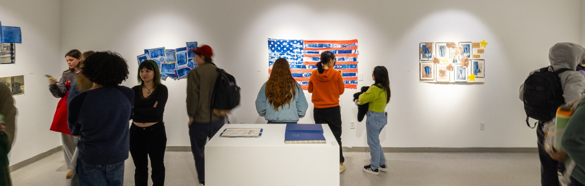 Students view photographs displayed on gallery walls during an ART 340 exhibition at the Center for the Arts, with multiple visitors gathered around the work.